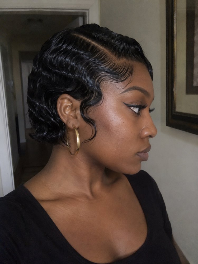 dark brown appears short length The hair is dark brown and appears to be short in length, reaching just above the nape of the neck. The texture is wavy and smooth, with a center part and two braids framing the face that transition into loose, crimped curls at the sides and back, and subtle baby hairs are visible along the hairline