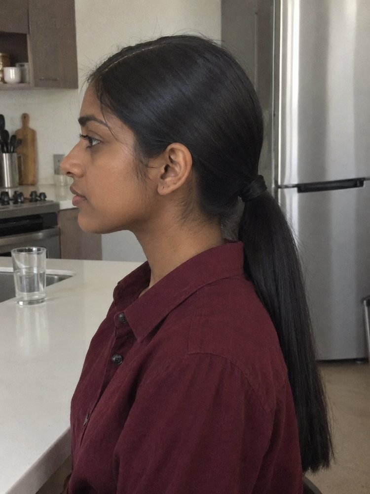 dark brown appears straight smooth The hair is dark brown and appears to be straight and smooth, with a sleek texture. It is styled in a low ponytail that falls down the back, reaching a considerable length that likely extends past the mid-back area. The hair color is uniform with visible highlights, lowlights, balayage or dimension, and there is apparent regrowth, toner or gloss.