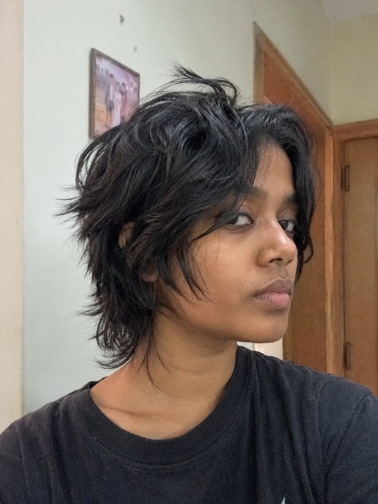 The hair is dark brown or black in color, with a medium length that falls around the chin and shoulders. The texture appears to be slightly wavy and piecey, with choppy layers that give it a lot of movement and texture, and some strands frame the face
