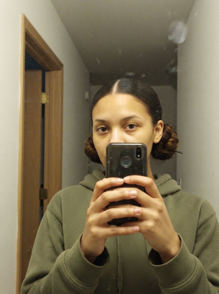 The hair is dark brown in color, pulled back into two low buns on either side of the head