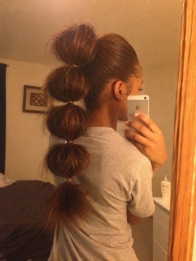 dark brown color subtle hints The hair is a dark brown color with subtle hints of lighter brown undertones, styled into a long, bubble-like ponytail secured with small hair ties