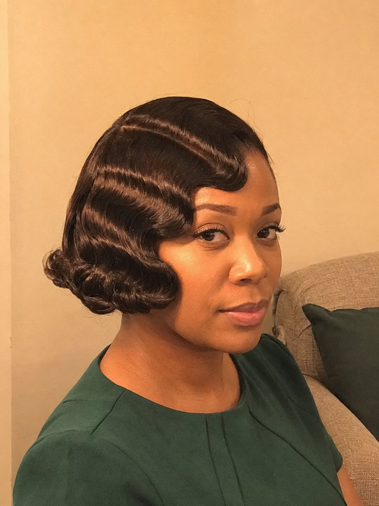 dark brown cut bob length The hair is dark brown, cut in a bob length, and features a vintage-inspired wave pattern. The texture appears smooth and sleek, with defined waves that add dimension to the overall style, and has a side part with deep finger waves that frame the face