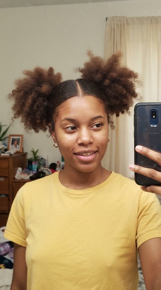 The hair is dark brown with a medium to tight curl pattern, styled into two puffy sections on either side of the head