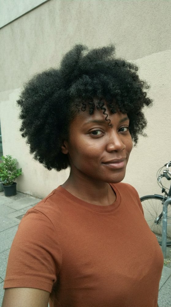The hair is dark brown with a natural texture that is tightly coiled and curly