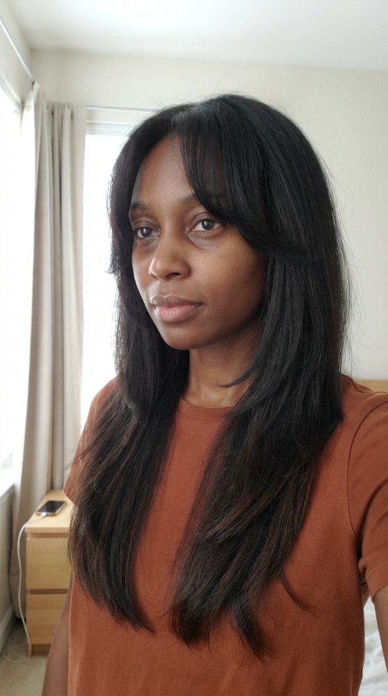 The hair is dark brown and reaches down to the mid-back area, with a straight cut style and subtle layers