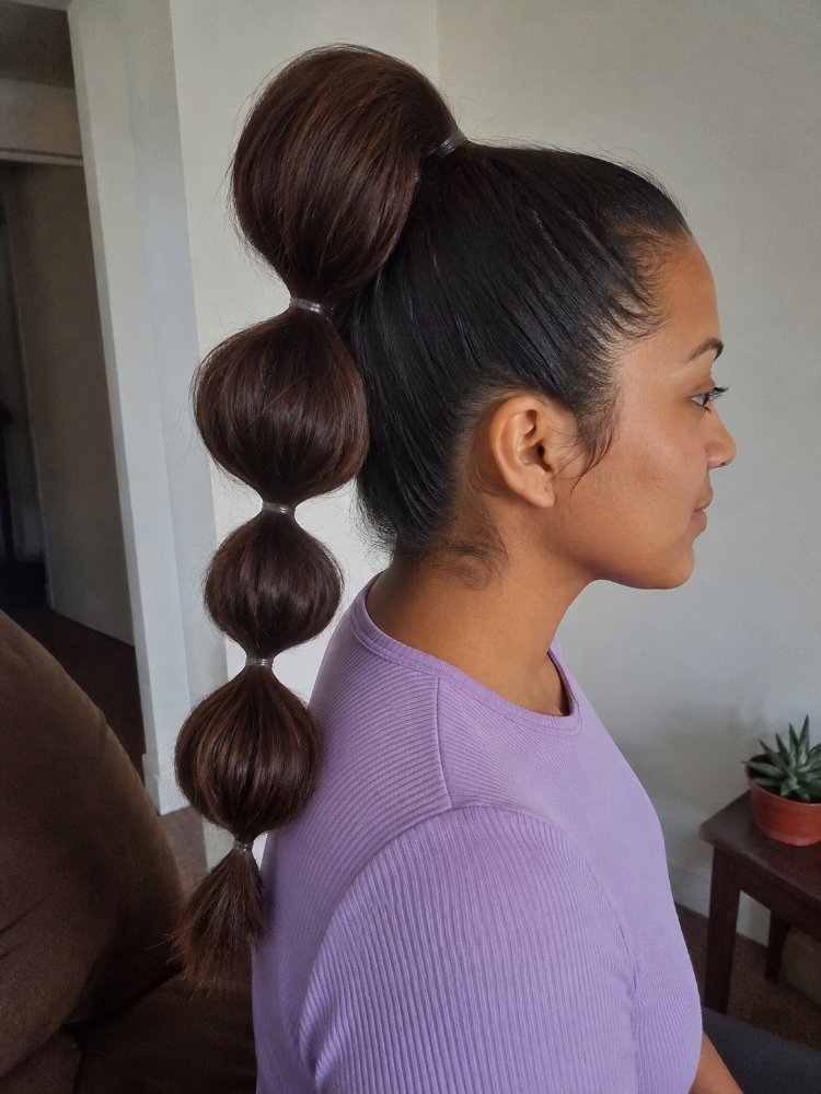 The hair is dark brown with a smooth, sleek texture and is styled in a unique bubble ponytail. The ponytail features four distinct sections, each secured with a small elastic band, creating a visually appealing, dimensional look with dimensional color, and apparent soft regrowth blending. The cut style appears to be long, with visible layers or face-framing elements, and there are curls or braids present