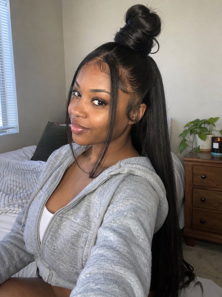 The hair is dark brown and straight with a high ponytail styled into a bun on top of the head, with the rest of the hair cascading down to a considerable length. The hair appears to have a sleek, smooth texture and a glossy finish, with visible highlights, lowlights, balayage or dimension; there is also visible regrowth, toners or gloss. The cut style features long layers that frame the face, with curls or braids present