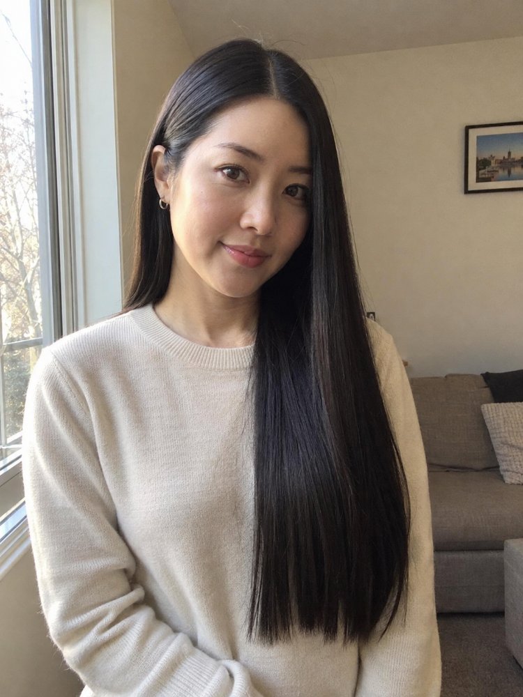 dark brown straight long reaching The hair is dark brown, straight, and long, reaching down to the mid-back area. It appears to be a solid, uniform color with subtle highlights, and has a smooth, sleek texture with discernible curls, braids or layers, framing the face with a center parting