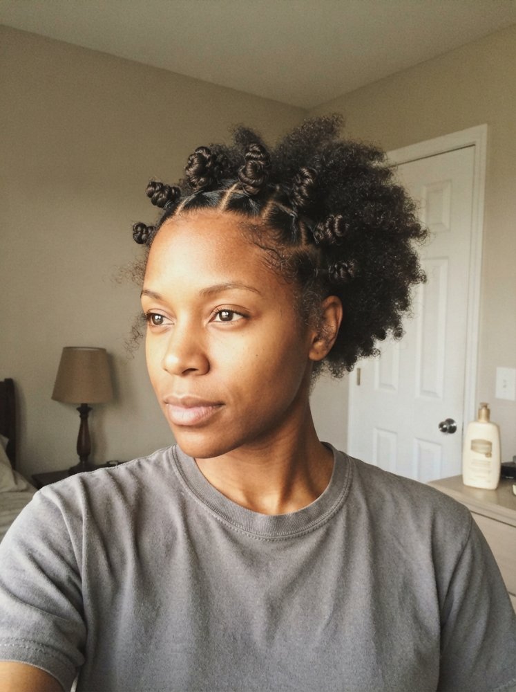 The hair is dark brown and styled in Bantu knots on top, with the rest of the hair pulled back into a puff.