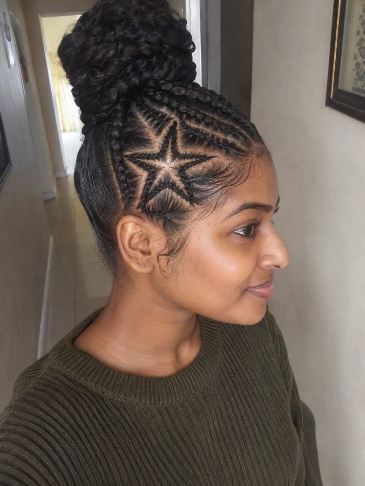 The hair is dark brown and styled in an intricate design, featuring a high bun and cornrows that form a star pattern on the side of the head. The hair is long, with the braided sections pulled back and secured into a high bun, and has a smooth, sleek texture with visible layers or curls. The hair color appears to be a single, rich brown shade with dimensional color, and there is visible regrowth or gray blending