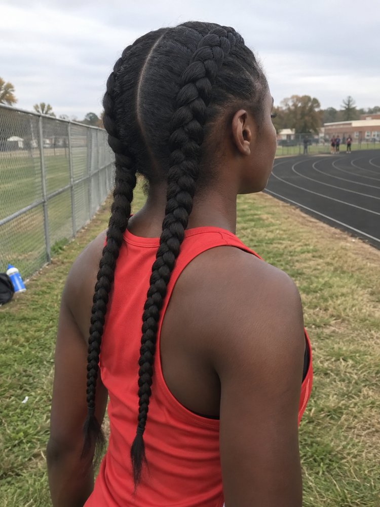 dark brown styled two long The hair is dark brown and styled in two long French braids that extend down the back, reaching a considerable length. The braids are smooth and sleek, with visible layers, curls or highlights, and appear to be a natural, unadorned style with signs of balayage, toner, gloss or blended color tones, and minimal natural color transition