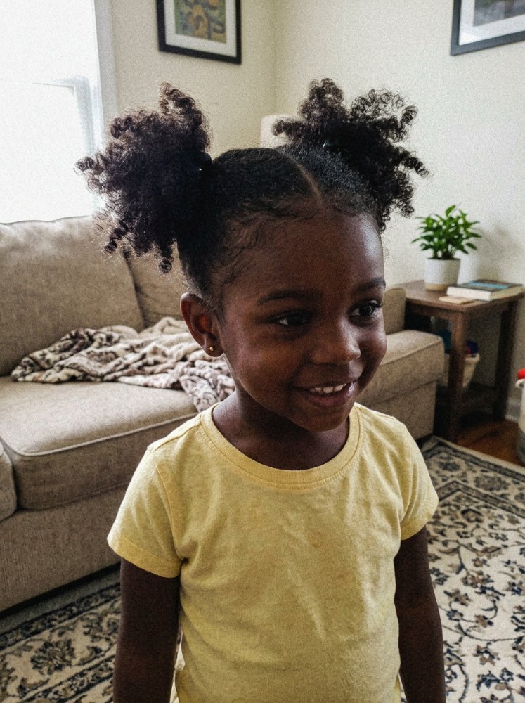 The hair is dark brown and styled in two puffy ponytails on top of the head