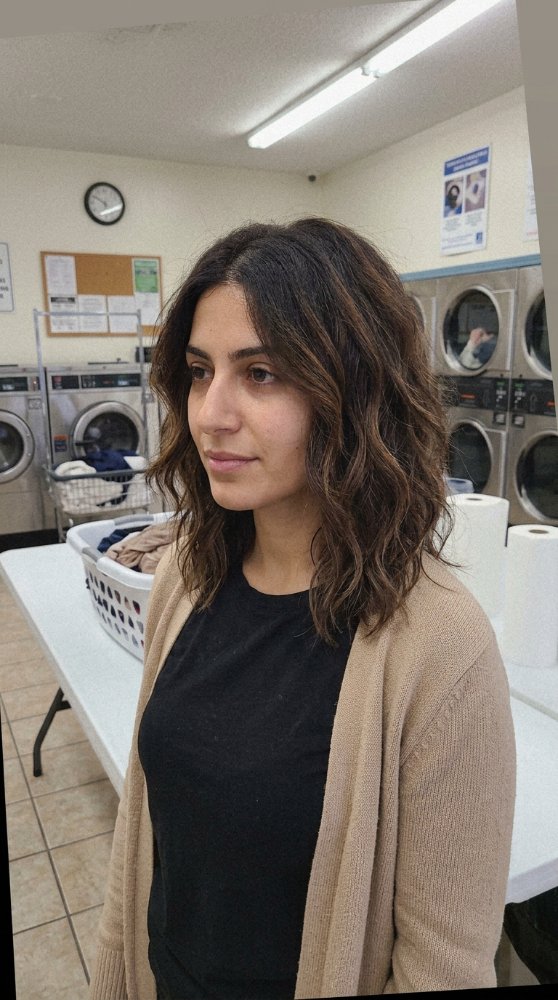 The hair is dark brown with subtle highlights, a medium to long length, reaching just below the shoulders