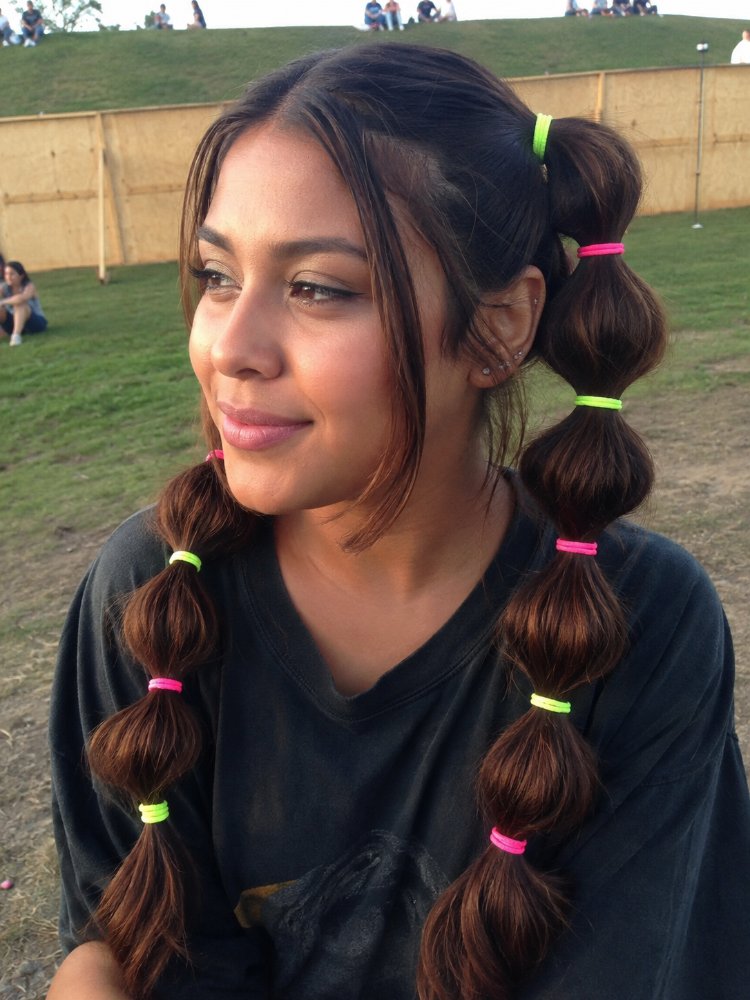 dark brown subtle hints lighter The hair is dark brown with subtle hints of lighter brown, likely from natural dimension or subtle highlights. It is styled in two long, thick braids with neon pink and green hair ties, and appears to be past shoulder length, possibly mid-back length. The texture seems smooth and healthy