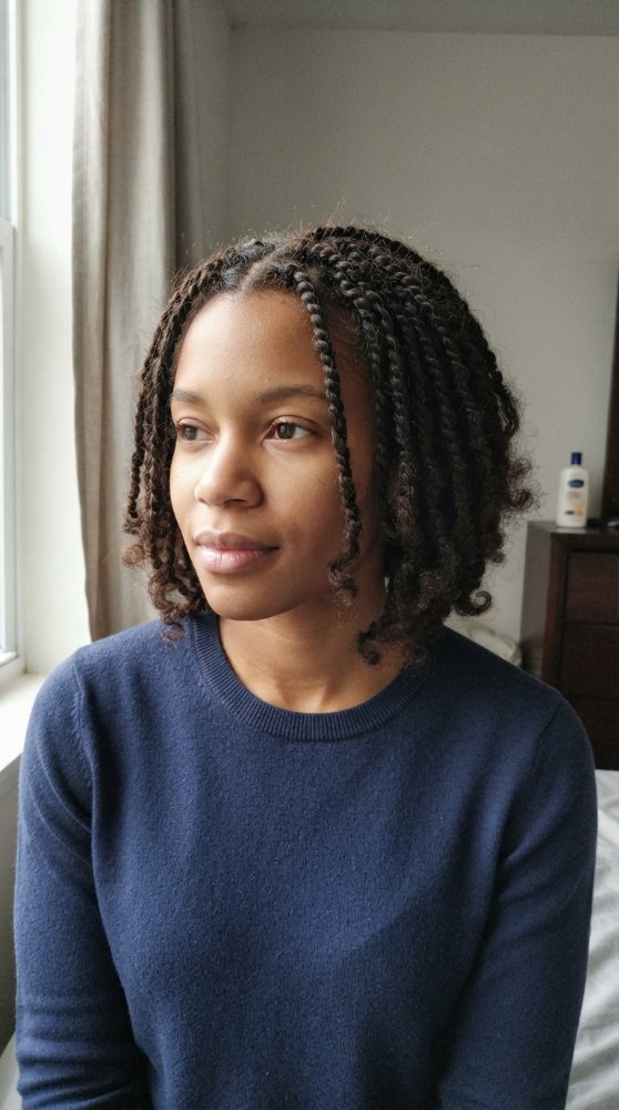 The hair is dark brown with a subtle sheen, styled in small, tight braids that fall just above the shoulders in length