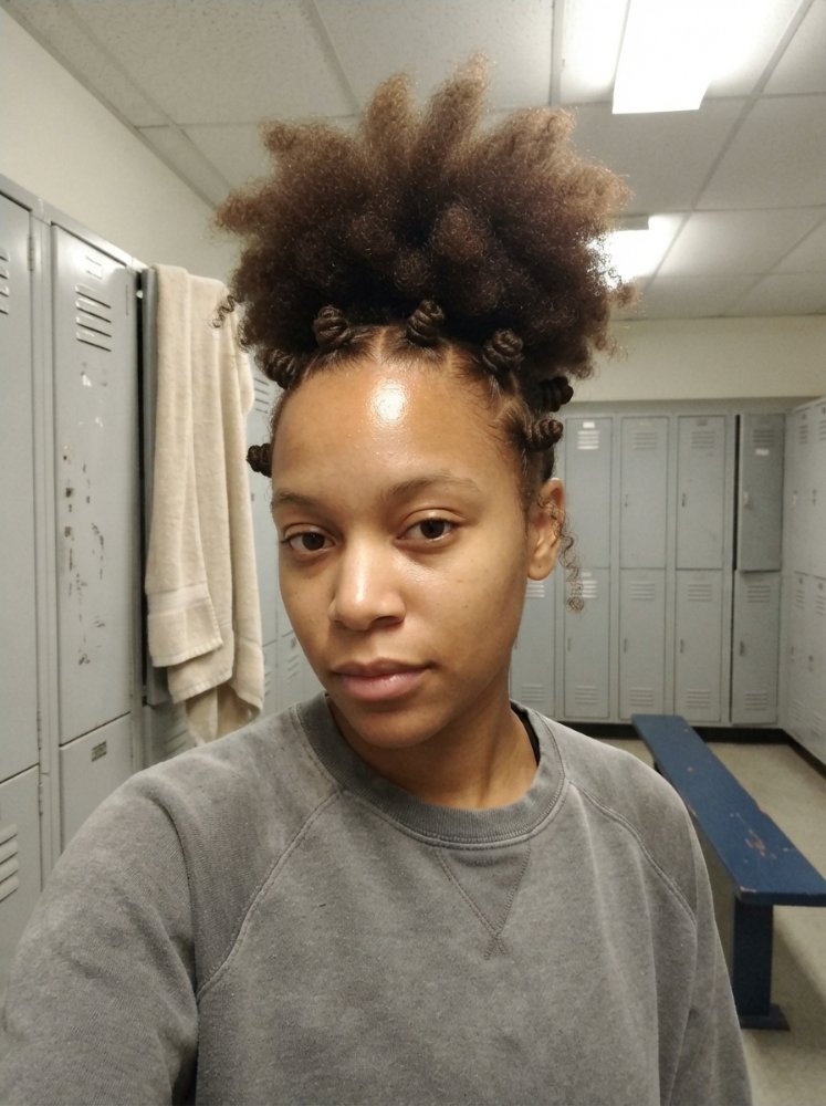 The hair is dark brown with a voluminous, curly texture and is styled in Bantu knots on top