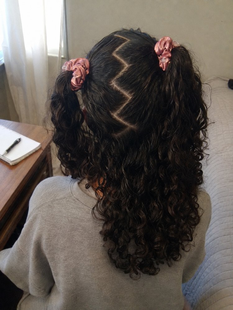 dark brown zig zag parting styled The hair is dark brown with a zig-zag parting and styled into two pigtails secured with pink scrunchies. The curly locks fall down to a medium length