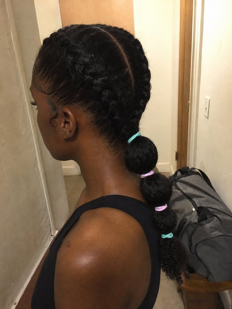 The hair is dark brown/black in color, smooth, and sleek, with a shiny texture. It is styled in two large French braids that are looped into bubble-like sections and secured with small elastic bands in pastel colors, with the ends left loose and curly. The hair appears to be long, reaching down to the middle of the back, with a simple and sleek cut style and visible layers or face-framing elements