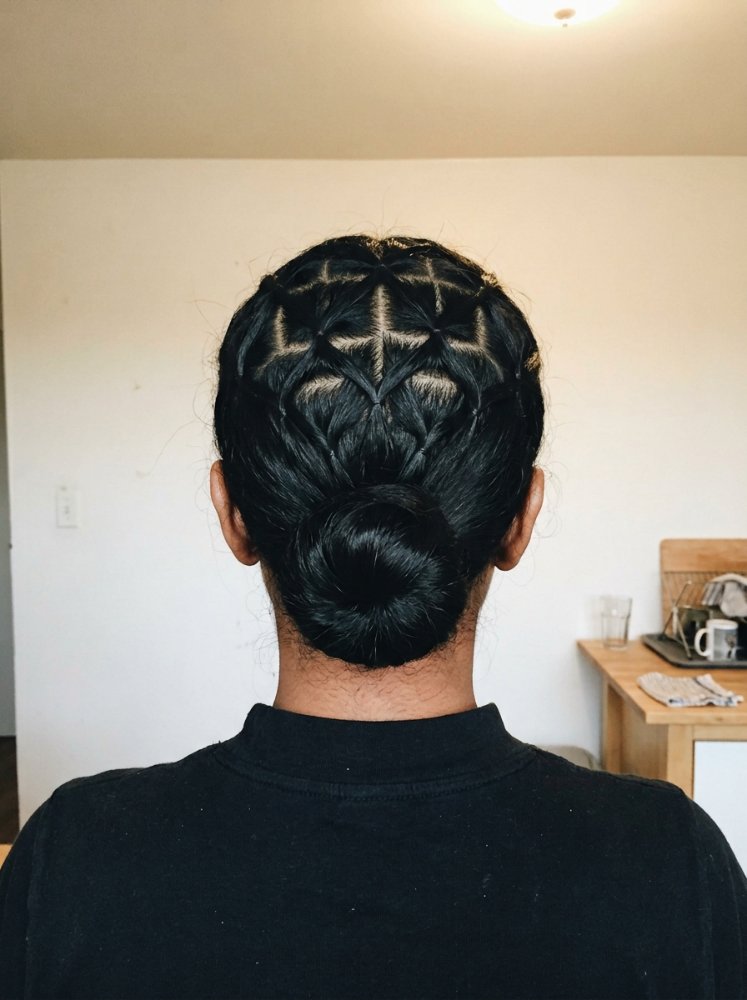 The hair is dark in color and styled in an intricate braided design that converges into a low bun