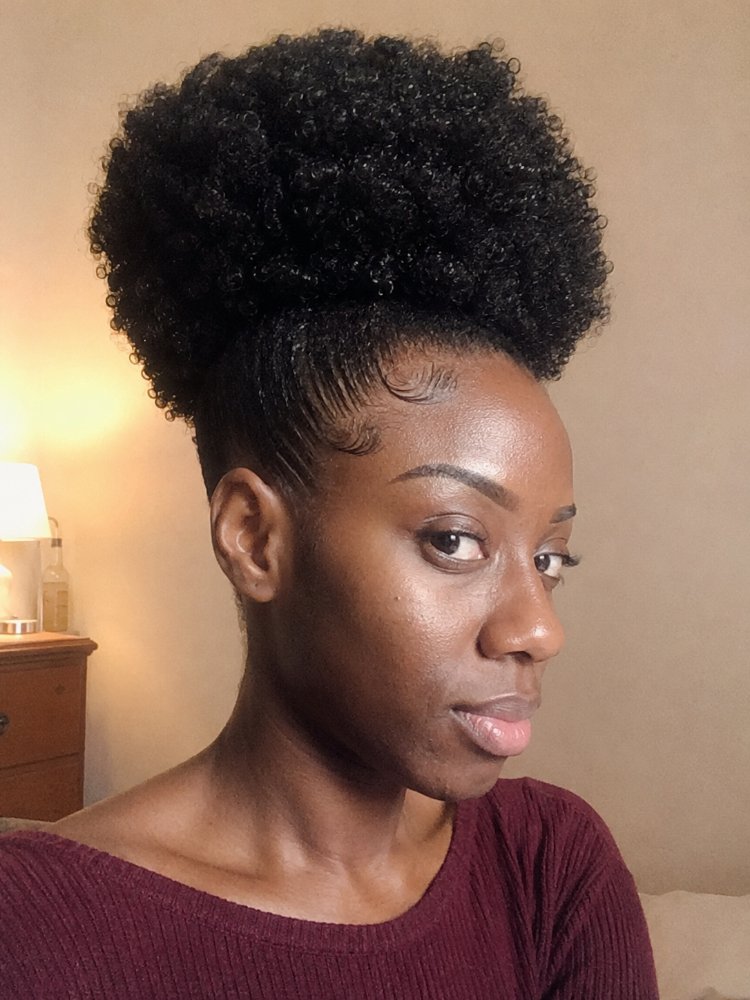 dark color tightly coiled highly The hair is dark in color, tightly coiled, and highly textured, forming a voluminous, curly puff on top of the head. The hairline has been styled with baby hairs, which are short, fine hairs that have been smoothed and shaped to frame the face