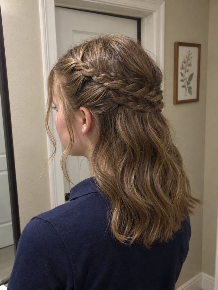light brown color subtle highlights The hair is a light brown color with subtle highlights, appearing to be a medium to long length, reaching down to the middle of the back. The hair has a wavy texture and features a crown braid that frames the head, with loose, flowing strands cascading down, and subtle dimension and layering visible throughout.