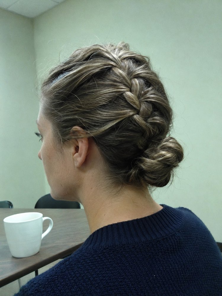 The hair is a light brown color with subtle highlights, styled in a braided updo that forms a low bun