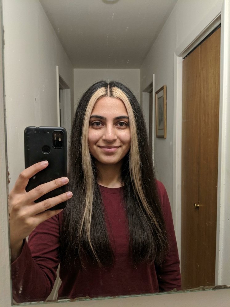 The hair is long, straight, and dark brown in color with a distinctive blonde streak running down the center, framing the face