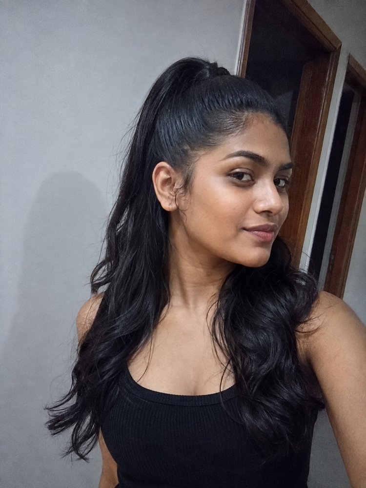 predominantly dark brown black color The hair is predominantly dark brown or black in color, with a smooth and sleek texture. It appears to be long, reaching down to the mid-back area, with loose, flowing waves at the ends and a high ponytail that adds dimension to the overall look. The hair has a glossy finish, suggesting it may have been styled with a toner or gloss
