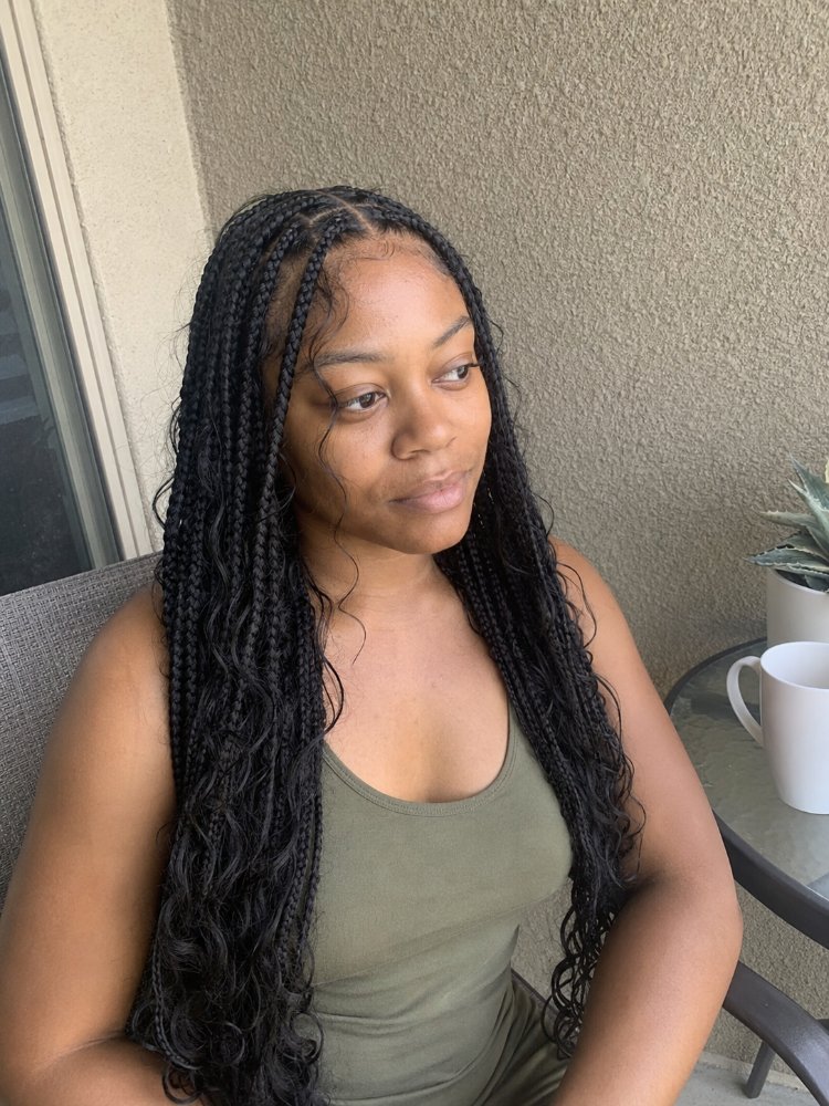 The hair is styled in long, small box braids that fall past the waist