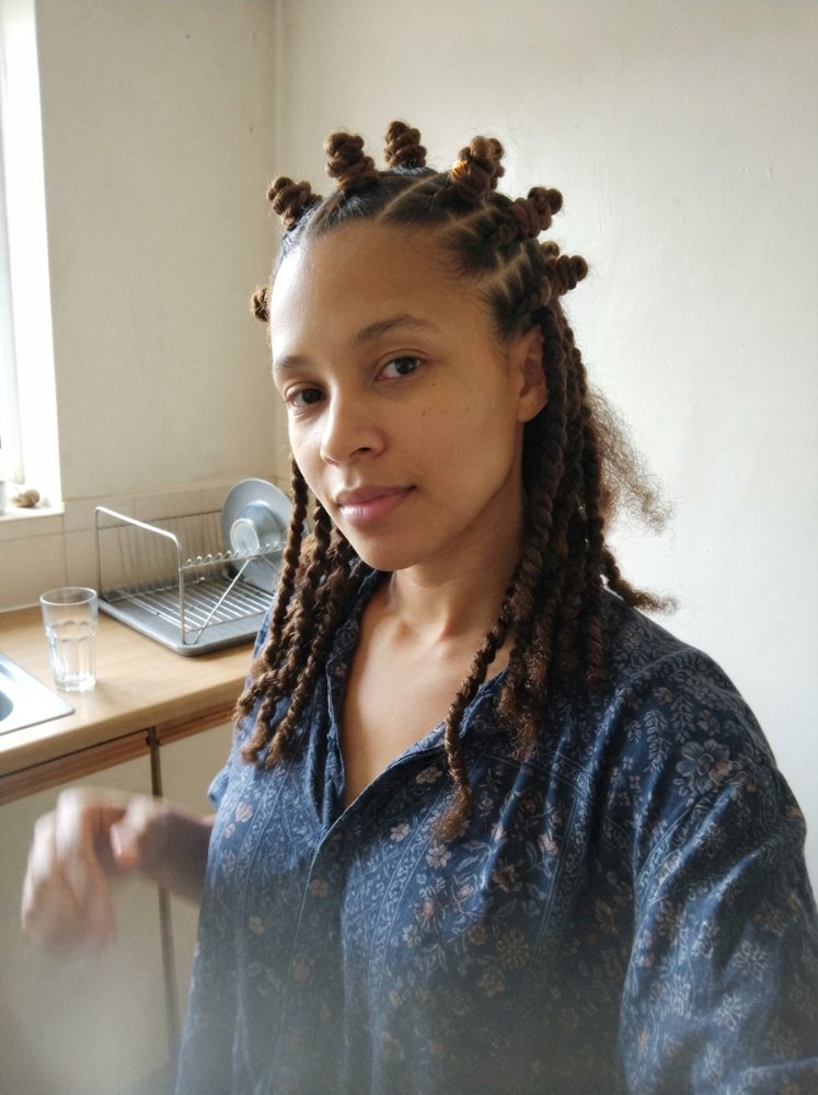 The hair is styled in long, thick, brown, spiral-shaped braids that fall down past the shoulders