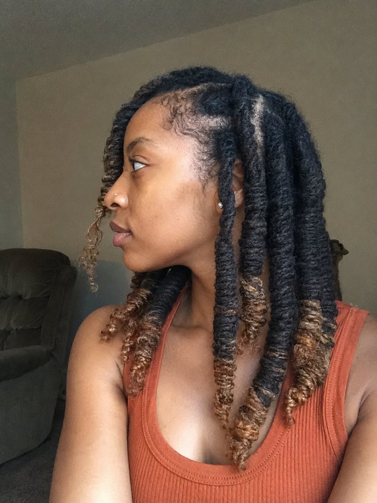 styled thick large long dreadlocks The hair is styled in thick, large, and long dreadlocks that fall past the shoulders. The hair is primarily dark brown/black with subtle ombre effects, showcasing lighter brown tones at the ends, adding dimension and a hint of balayage technique. The texture appears coarse and tightly coiled