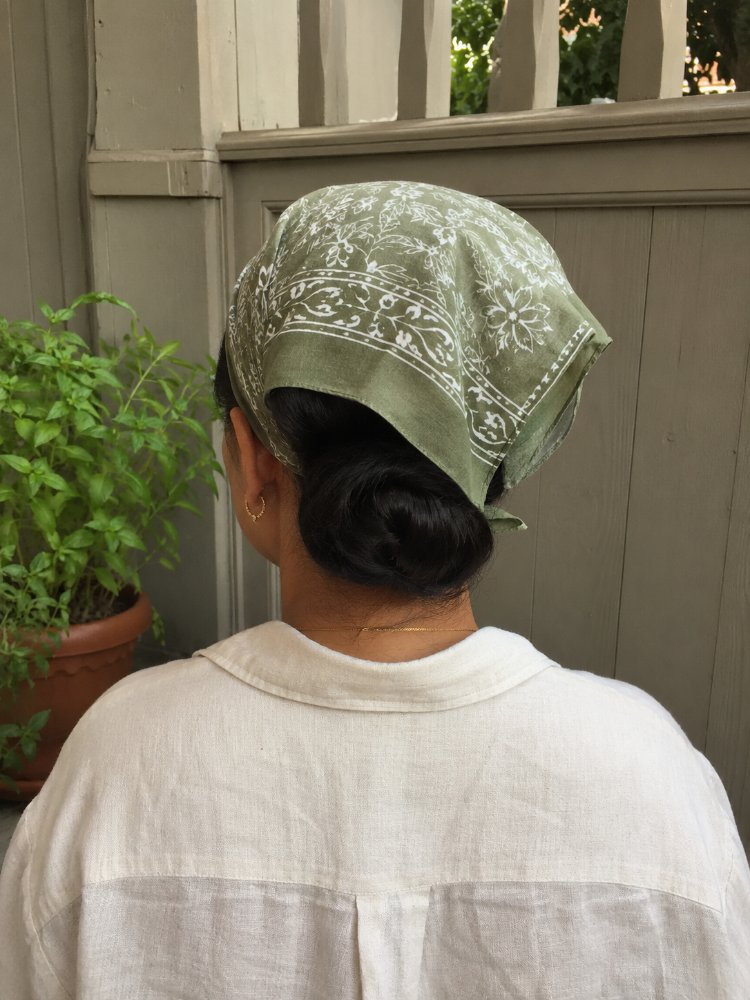 visible dark color styled low dark in color and styled into a low bun. The texture appears smooth and sleek, with visible curls, braids or layers. A green headscarf covers most of the hair, but it seems to be neatly tucked away, with stray hairs
